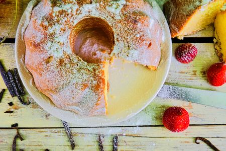 Old fashioned sand cake with cup of black tea and pieces of vanilla on wooden background. Egg-yolk sponge cake with stawberries on rustic white backgroundの写真素材