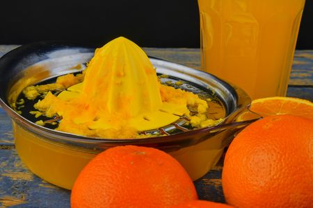 Tangerines, oranges, a glass of orange juice and manual citrus squezeer on blue wooden background....