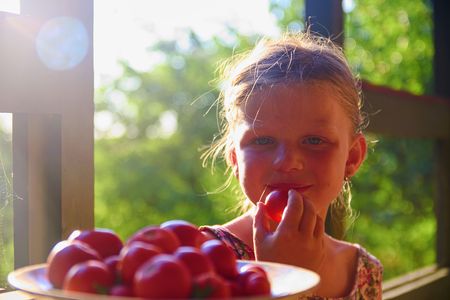Little girl sitting on porch in summer. Tomatoes on plate. Dreamy and romantic image. Summer and happy childhood conceptの写真素材