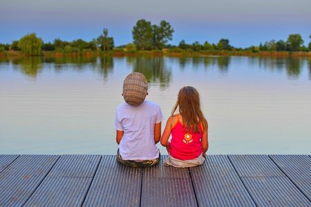 Little boy and girl sitting on wooden pier with. Love, friendship and childhood concept. Beautiful romantic sunset picture.  Copy spaceの写真素材
