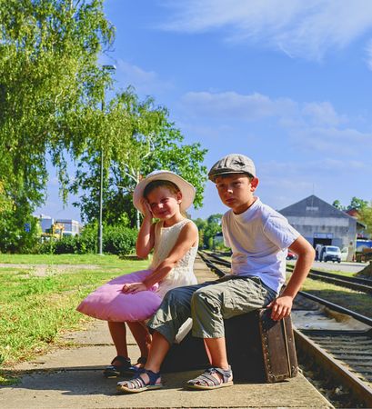 Adorable little girl and boy on a railway station, waiting for the train with vintage suitcases. Traveling, holiday and chilhood concept. Travel insurance concept. Vacation trip.の写真素材
