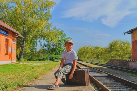 Little boy  on a railway station, waiting for the train with vintage suitcase. Traveling, holiday and chilhood concept. Travel insurance concept. Travel, tourism, summer vacation and family concept.の写真素材