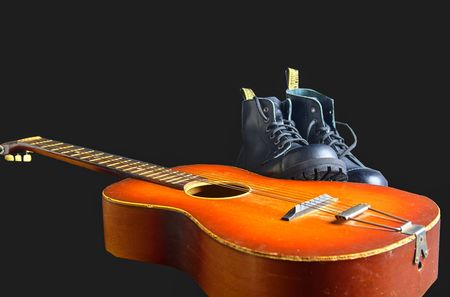 Rock and roll concept. Black boots and acoustic guitar. Rock and roll boots on black backgroundの写真素材