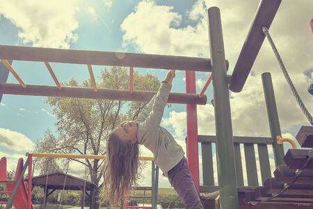 Little girl playing on playground, hanging walk along the monkey bars.