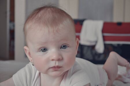 Charming blue-eyed baby girl, 6 months old, crawled in bed. Baby girl wearing a bodysuit
