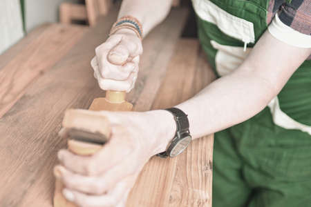 Close up of a carpenter planing a plank of wood with a hand plane. Carpenter working with plane on wooden background. Young carpenter wearing braceletsの写真素材