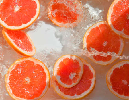Slices of grapefruit in water on white background. Grapefruit close-up in liquid with bubbles. Slices of blood red ripe grapefruit in water. Macro image of fruits in waterの写真素材