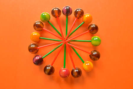 Various colorful lollipops on pastel background. Bright juicy colored lollipops on an orange background. Lollipops in the form of a flower. Fruit candyの写真素材