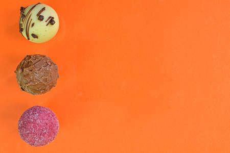 Chocolate bonbons or pralines on orange pastel background. Assortment of chocolate pralines on orange background with copy space. Flat lay, top viewの写真素材
