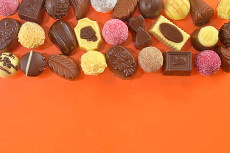 Chocolate pralines frame top view stock images. Chocolate candies on an orange background. Chocolate...