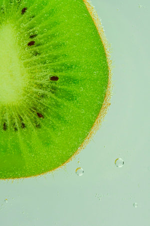 Fresh kiwi fruit slice in liquid with bubbles. Close-up of a kiwi fruit slice in soda water. Bubbles on kiwi fruit. Slice of kiwi fruit in carbonated water. Macro vertical image.の写真素材