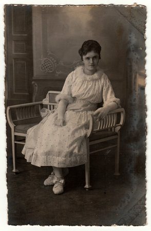 GERMANY - CIRCA 1920s: Vintage photo shows woman sits on a white period bench. Retro black and white studio photography.のeditorial素材