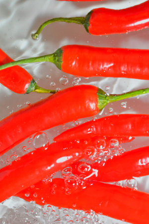 Red chili peppers close-up in liquid with bubbles. Slices of red chili peppers in water. Close-up of red chili peppers on white background. Vertical and macro image.の写真素材