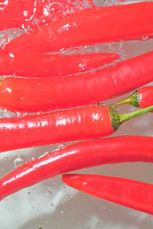 Red hot peppers in water splash on white background. Splashing water and bubbles. Vertical image, close-upの写真素材