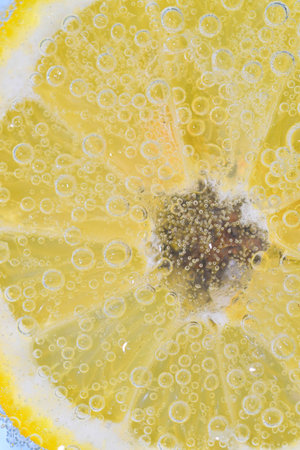 Close-up of a lemon slice in liquid with bubbles. Slice of ripe lemon in water. Close-up of fresh lemon slice covered by bubbles. Macro vertical imageの写真素材
