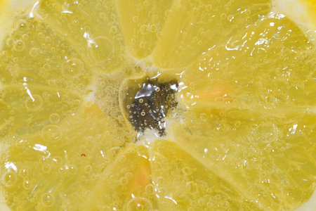 Close-up of a lemon slice in liquid with bubbles. Slice of ripe lemon in water. Close-up of fresh lemon slice covered by bubbles. Macro horizontal imageの写真素材