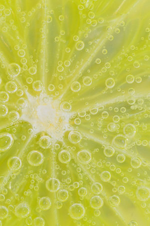 Close-up of a lime slice in liquid with bubbles. Slice of ripe lime in water. Close-up of fresh lime slice covered by bubbles. Macro vertical imageの写真素材
