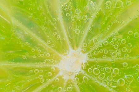 Close-up of a lime slice in liquid with bubbles. Slice of ripe lime in water. Close-up of fresh lime slice covered by bubbles. Macro horizontal imageの写真素材