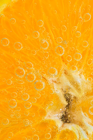 Slice of ripe orange fruit in water. Close-up of orange fruit in liquid with bubbles. Slice of ripe orange fruit in sparkling water. Macro image of fruit in carbonated waterの写真素材