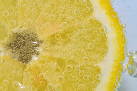 Slice of ripe lemon in water on white background. Close-up of lemon in liquid with bubbles. Slice of ripe lemon in sparkling water. Macro image of fruit in carbonated waterの写真素材