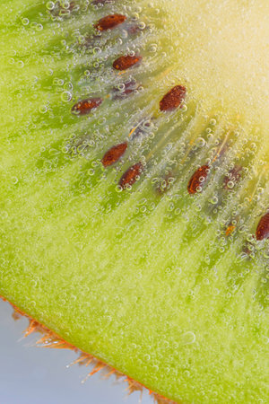 Close-up of a kiwi fruit slice in liquid with bubbles. Slice of ripe kiwi fruit in water. Close-up of fresh kiwi slice covered by bubbles. Macro vertical imageの写真素材