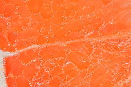Close-up of a grapefruit slice in liquid with bubbles. Slice of ripe grapefruit in water. Close-up of fresh grapefruit slice covered by bubbles. Macro horizontal imageの写真素材