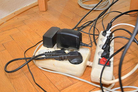 Cable chaos clutter from multiple electric wire extension cords and multi-contact plugs on wooden floor. Tangled cables on the parquet floor.の写真素材