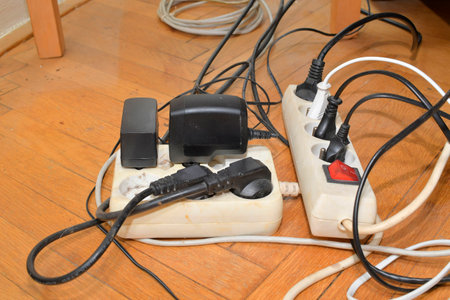 Tangled cables on the parquet floor. Overloaded electrical boards on the wooden floor. Electrical cables in disorder.の写真素材