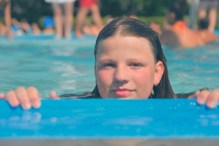 A picture of a little girl at a swimming pool in summer. A young girl looking over the edge of a...