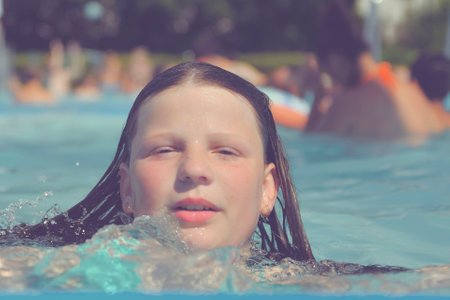 A picture of a little girl at a swimming pool in summer. A small girl swimming to the edge of a swimming pool at a swimming pool. Concept of summer, water fun, sun and relaxationの写真素材