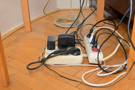 Cable chaos clutter from multiple electric wire extension cords and multi-contact plugs on wooden floor. Tangled cables on the parquet floor.の写真素材