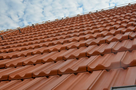 Newly covered roof. New roof covering with red clay tiles. Industrially manufactured tiles on the new roof. Concept of construction, building work, and renovation of the house.の写真素材