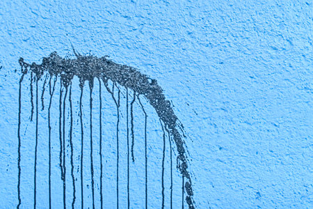 The harsh texture of a dark blue wall with a significant stain. The rough texture of a dark blue wall with an ink spot. The concept of background and textured surface.