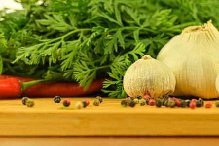 A bulb of garlic, red chili peppers, four-color pepper, and carrot tops on a wooden cutting board. The concept of cooking and vegetables in the home.の写真素材