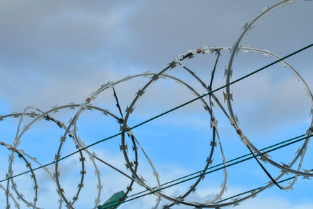 Barbed razor wire on a high-security building. Barbed wire and heavy wire fencing. Design of prisons, military facilities, nuclear power plants, and defense against illegal migration.の写真素材