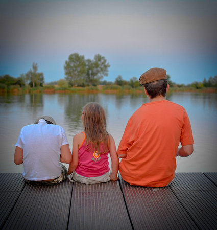 Children sitting on pier. Three children of different age - teenager boy, elementary age boy and...