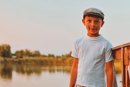 A smiling boy stands on a pier at the edge of a pond. The concept of summer holidays, carefree days,...
