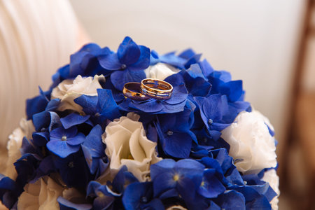 Gold rings on wedding bouquet of blue and white fresh flowers