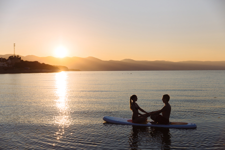 Silhouettes of perfect couple engage standup paddle boardingの写真素材