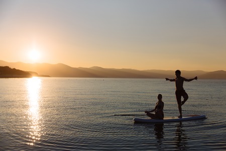 Silhouettes of perfect couple engage standup paddle boardingの写真素材