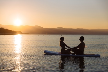 Silhouettes of perfect couple engage standup paddle boardingの写真素材