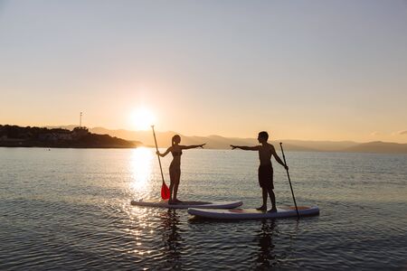 Silhouettes of perfect couple engage standup paddle boardingの写真素材