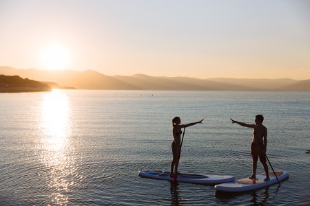 Silhouettes of perfect couple engage standup paddle boardingの写真素材