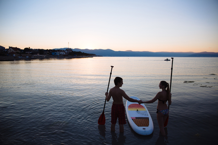 Silhouette of beautiful couple with sup surf and paddle at the ocean. Concept of lifestyle, sport, loveの写真素材