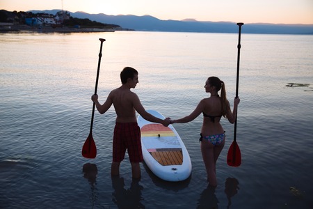 Silhouette of beautiful couple with sup surf and paddle at the ocean. Concept of lifestyle, sport, loveの写真素材