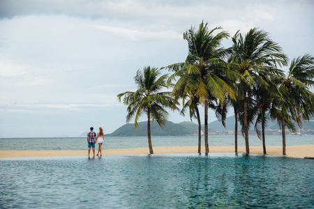 Just married couple hold each others hands, turned back stand and look at the sea. Palms on backgroundの写真素材