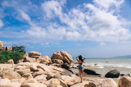 sexy girl in shorts and a swimsuit standing on the background of the sea rising herb. beautiful landscape with big stonesの写真素材