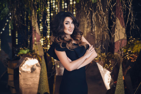 portrait of young beautiful brunette girl with long hair in a black dress posing in loft interior...