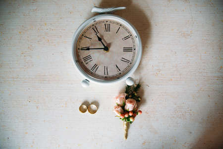 Wedding accessories. Boutonniere, Golden rings, a beautiful bouquet of flowers on white textured table. Concept of bride and groom ornamentationの写真素材