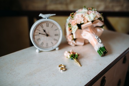 Wedding accessories. Boutonniere, Golden rings, a beautiful bouquet of flowers on white textured table. Concept of bride and groom ornamentationの写真素材